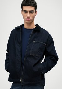 Tamsaus džinsinio audinio striukė su užtrauktuku, apykakle ir krūtine kišene. Siūlo laisvą siluetą ir subtilius siuvinėjimo akcentus.