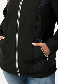 Černá bunda s prošívanými bočními panely, s bílým zipem a dvěma předními kapsami. Měkký materiál s hladkým povrchem.