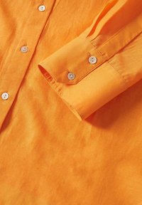 Chemise à manches longues orange vif avec des boutons blancs et un poignet boutonné visible sur le côté droit.