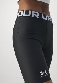 Czarne spodenki sportowe z wysokim, elastycznym paskiem w talii z napisem "UNDER ARMOUR" w kolorze białym. Gładki materiał z dopasowanym krojem i detalem z logo.