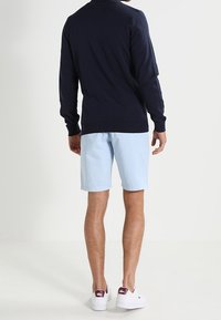 Marinblå tröja, ljusblå shorts och vita sneakers med lila detaljer. Tröjan har långa ärmar, rund hals och ribbad kant.