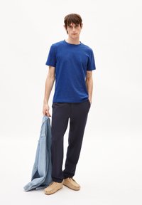 Blauwe T-shirt met korte mouwen, marineblauwe broek, beige schoeisel, met een lichtblauwe spijkerjack in de hand. Smooth textuur, casual pasvorm, minimalistisch design.