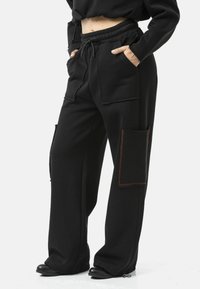 Zwarte joggingbroek met een ontspannen pasvorm, voorzien van voorzakken, contrasterende stiksels en een trekkoord in de tailleband. Gladde stoftextuur.