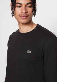 Sort langærmet t-shirt lavet af bomuld, med en rund hals og et lille grønt og rødt broderet krokodillelogo på brystet.