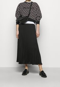 Czarna długa spódnica w połączeniu z wzorzystym czarno-białym swetrem. W zestawie torba na ramię i czarne buty z frędzlami.