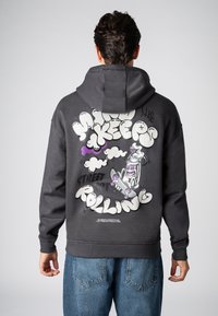 Grijze hoodie met capuchon, voorzien van een grote grafische print in wit, paars en zwart op de achterkant, met daarop een skateboarder en gestileerde tekst.