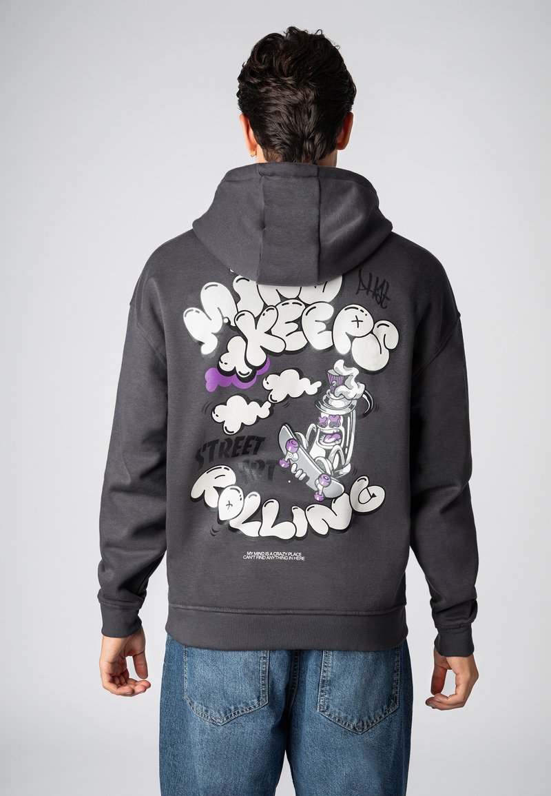 Grijze hoodie met capuchon, voorzien van een grote grafische print in wit, paars en zwart op de achterkant, met daarop een skateboarder en gestileerde tekst.