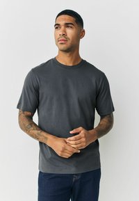 Tumši pelēks īsvasarā krekls kokvilnas maisījumā, ar apaļu kakla izgriezumu un gludu tekstūru, kombinēts ar tumšiem denima džinsiem.