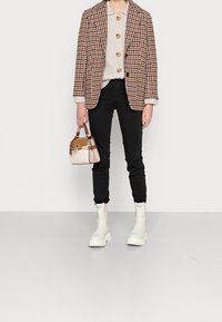 Kostkovaný blejzr v hnědé barvě, oversized střih, zkombinovaný s texturovaným krémovým svetr a přiléhavými černými kalhotami. Bílé mohutné boty a malá dvoubarevná kabelka.