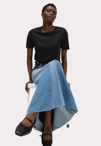 T-shirt nera a maniche corte abbinata a una gonna di jeans con un design svasato e orlo sfrangiato. Scarpe nere con dettagli strap.