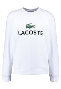 Biała bluza z mieszanki bawełny, z zielonym logo krokodyla i napisem "LACOSTE" w grubym czarnym kroju pisma. Mankiety i dół bluzy wykończone ściągaczem.