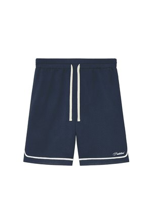 Male wearing navy mesh shorts with beige trim, white logo socks, and beige suede lace-up shoes, standing against a plain background.