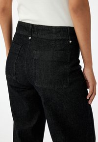 Zwarte denim jeans met een aangesloten taille, twee achterzakken en subtiele stiksels. De stof heeft een gladde textuur met een lichte glans.