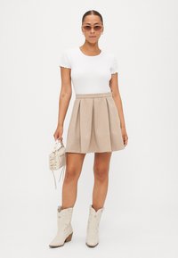 Top blanco ajustado con mangas cortas, falda plisada color beige, botas vaqueras color crema con acentos florales, pequeño bolso beige.