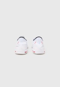 Ζεύγος λευκών αθλητικών παπουτσιών με κόκκινες λεπτομέρειες, απεικονιζόμενα από πίσω, σε απλό γκρι φόντο.