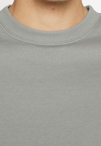 Suéter de algodón gris de manga larga con textura sutil. Cuello redondo y bordes bien cosidos sin logotipos ni gráficos visibles.