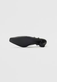 Chaussure à talon noir avec une texture lisse, un bout pointu et un talon fin. Présente un coussin de pied doux et un design minimaliste, mettant en valeur la forme et la silhouette.