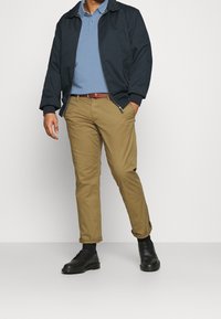 Marinblå bomberjacka över en ljusblå polo, ihop med beiga chinos och svarta läderskor, framhävd av ett brunt bälte.