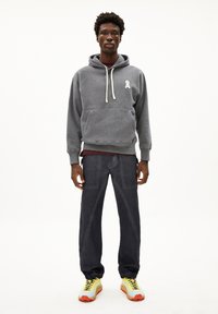 Grijs hoodie sweatshirt met wit logo, gecombineerd met donkere broek en veelkleurige sneakers. Vlotte textuur en ontspannen pasvorm.