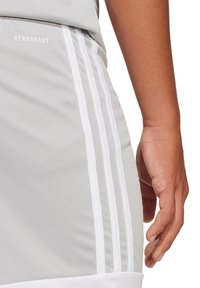 Shorts de sport gris avec des bandes blanches sur les côtés, marque AEROREADY, fabriqués en tissu respirant ; taille élastique, texture lisse.
