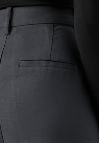 Pantalons taillés gris foncé avec une texture de tissu lisse, présentant une poche arrière rectangulaire sans matériel ou embellissements visibles.