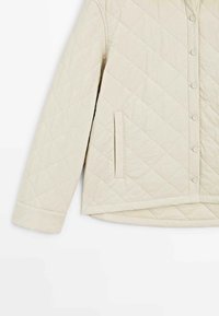 Světlá béžová prošívaná bunda s knoflíkovým zapínáním, bočními kapsami a zakulaceným lemem. Hladká textura s diamantovým prošitím.