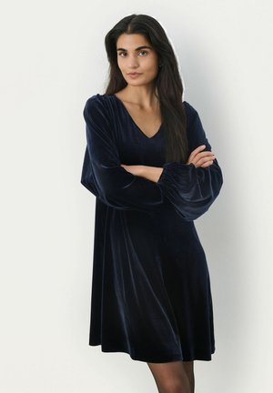 Robe en velours bleu marine avec un décolleté en V, des manches longues bouffantes et une coupe décontractée, dotée d'une texture lisse et d'un ourlet à mi-genoux.
