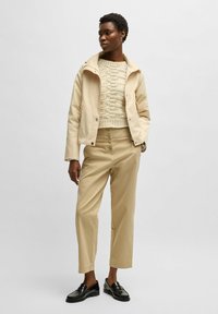 Beige kort jacka över en strukturerad stickad krämfärgad tröja, i kombination med högmidjade beige byxor och svarta loafers. Enkla linjer och neutrala färger.