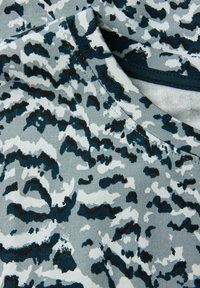 Lähellä otettu kuva taitetusta kankaasta, jossa on harmaa, valkoinen ja musta abstrakti maastokuvio sekä näkyvät ompeleet sauman kohdalla.