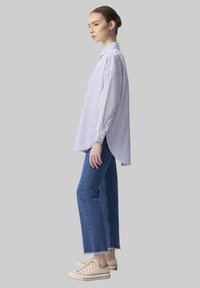 Cămașă cu dungi, albă și albastră, dintr-un material lejer, cu mâneci lungi. Asortată cu blugi drepti, cu talie înaltă, din denim și tenisbeige.