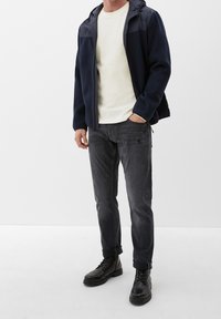 Giacca in pile della marina con cappuccio, camicia bianca testurizzata, jeans grigio scuro e stivali neri stringati. Taglio dritto e design casual.
