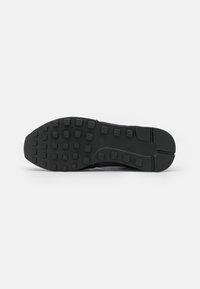 Suola di scarpa nera con motivi di grip testurizzati, forma piatta e leggera curvatura nella punta. Realizzata in gomma con dettagli a linee definite.