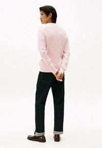 Maglione a trecce rosa chiaro con polsini e orlo a costine, abbinato a jeans scuri e mocassini marroni, visto da dietro.