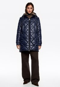 Tmavomodrý prešívaný puffa kabát s kapucňou, funkčným predným zipsom, bočnými vreckami a rebrovanými manžetami. Mäkka textúra s lesklým povrchom.