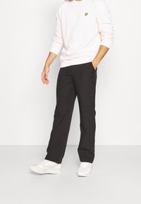 Felpa rosa chiaro con maniche a cuffia, logo giallo sul petto, abbinata a pantaloni neri a gamba dritta e sneakers bianche.