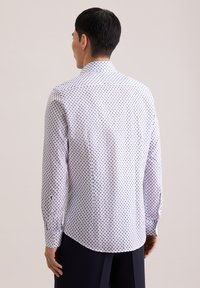 Camicia a maniche lunghe in tessuto bianco con motivo a pois blu, dotata di colletto classico e polsini con bottoni. Vista posteriore con vestibilità sagomata.