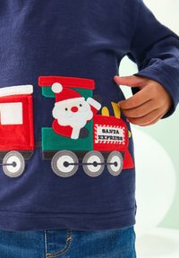 Marinblå långärmad skjorta med ett broderat tågmotiv som visar tomten, röda och gröna färger samt texten "SANTA EXPRESS" på tågvagnen.