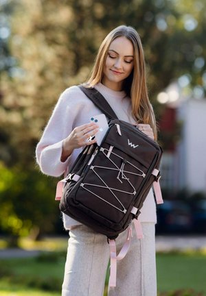 Schwarzer Rucksack mit pinkfarbenen Akzenten und elastischem Kordeldetail. Er verfügt über mehrere Fächer und wird von einer Person gehalten, die gerade ein Telefon herausnimmt.