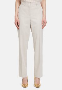 Beige, hoge taille broek met een gestructureerde afwerking, met rechte pijpen en persplooien, gecombineerd met gouden, spitse hakken.