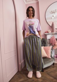 Lilac t-shirt with graphic of boots and flowers, paired with grey striped trousers in green and yellow, and pink quilted slippers.