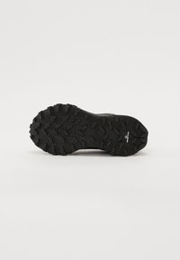 Semelle de chaussure de sport noire avec des crans profonds pour une traction, présentant une surface en caoutchouc texturée et des crampons distincts pour une prise améliorée.