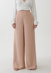 Vida stora byxor i mjukt rosa tyg, hög midja med en slät yta, tillsammans med en vit långärmad topp. Inga synliga knäppningar.