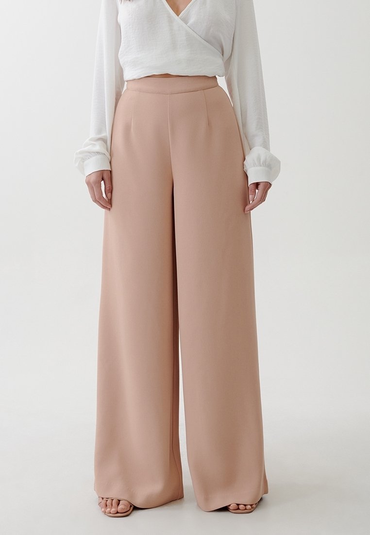 Vida stora byxor i mjukt rosa tyg, hög midja med en slät yta, tillsammans med en vit långärmad topp. Inga synliga knäppningar.