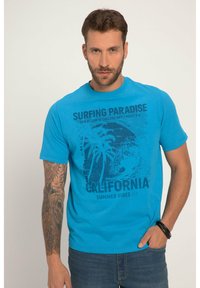 Modrá bavlněná tričko s grafickým potiskem, který zobrazuje palmy a text "Surfing Paradise California" ve tmavě modré barvě. Krátké rukávy, kulatý výstřih.