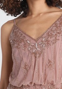 Beaded top in blush pink sheer fabric, featuring a V-neckline and intricate floral embroidery with sequins and delicate pleating along the hem.