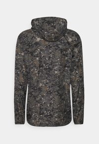 Kurtka z kapturem w ciemnym kamuflażu, w odcieniach szarości, brązu i czerni; wykonana z lekkiej, teksturowanej tkaniny.