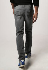 Jeans in denim grigio con taglio dritto, dotati di tasche posteriori e una texture leggermente usurata. Abbinati a sneakers blu e bianche.