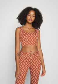 Top cropped em cor ferrugem com padrão de ondas brancas, decote quadrado e alças grossas. Combinado com calças de cintura alta com design semelhante.