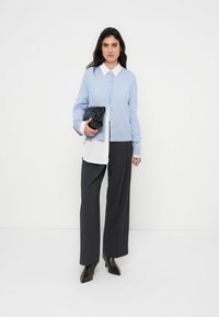 Ανοιχτό μπλε ζακέτα με κουμπιά, λευκό πουκάμισο με ρίγες από κάτω, σκούρο παντελόνι με φαρδιά μπατζάκια και μαύρο τσαντάκι χειρός. Φοράει μαύρα μυτερά μποτάκια.