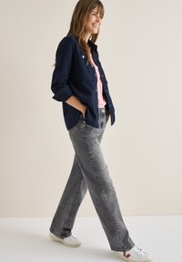 Camisa azul marino, top rosa y jeans de mezclilla gris. Calzado casual con base blanca y acentos rojos. Modelo caminando frente a un fondo neutro.